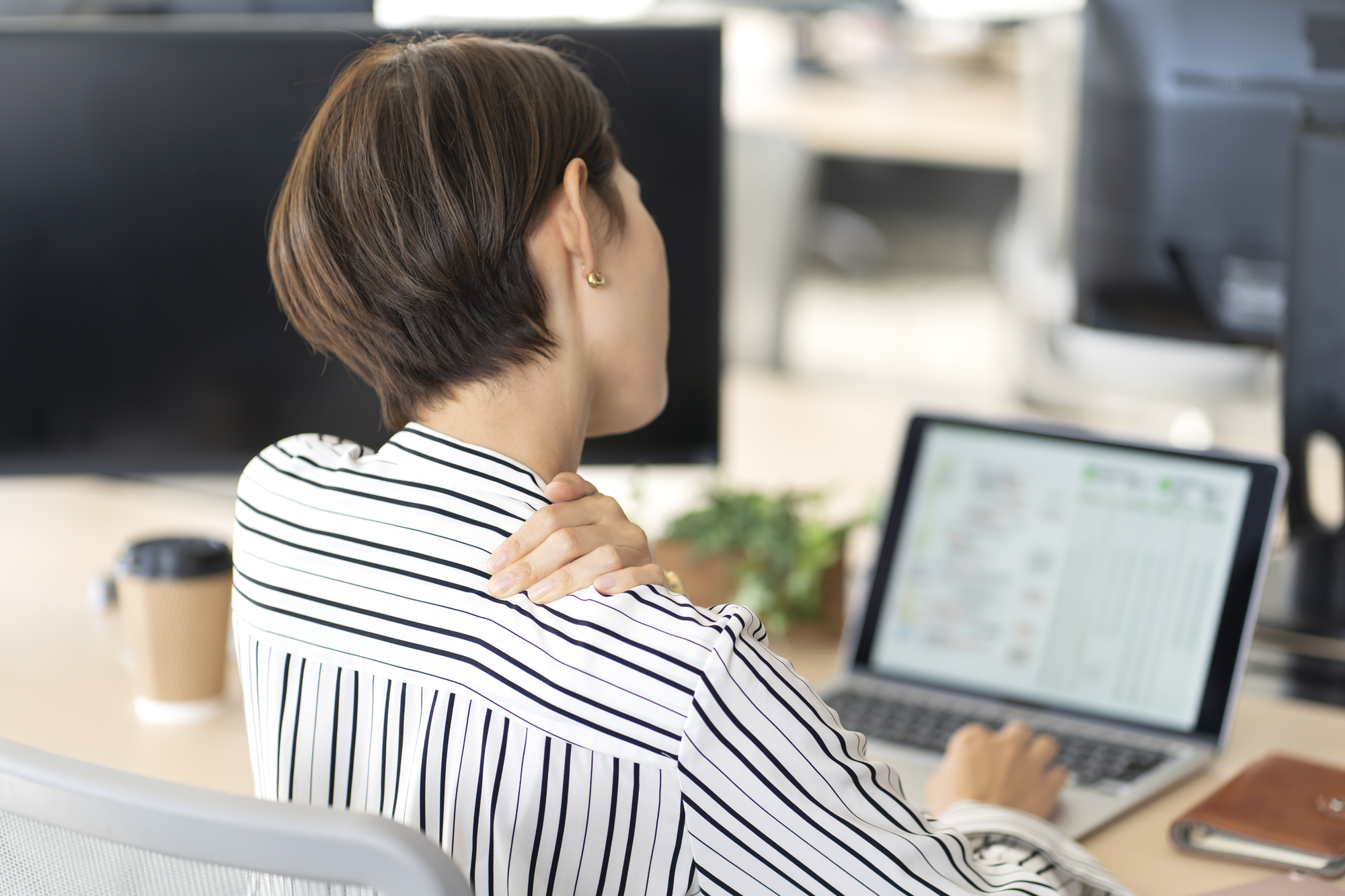 パソコン作業中に肩を押さえる女性